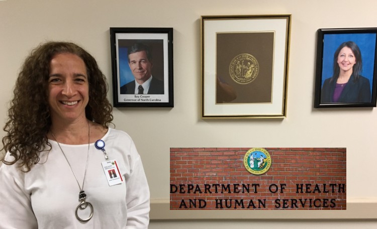 Dr. Jessie Tenenbaum, PhD at NCDHHS with framed photos of Gov. Roy Cooper and NCDHHS Secretary Mandy Cohen, MD, MPH