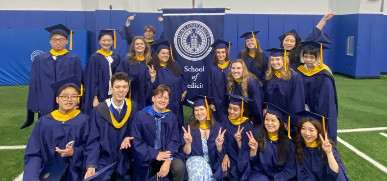 Students in their graduation regalia standing in front of a podium with the Duke Seal on it. 