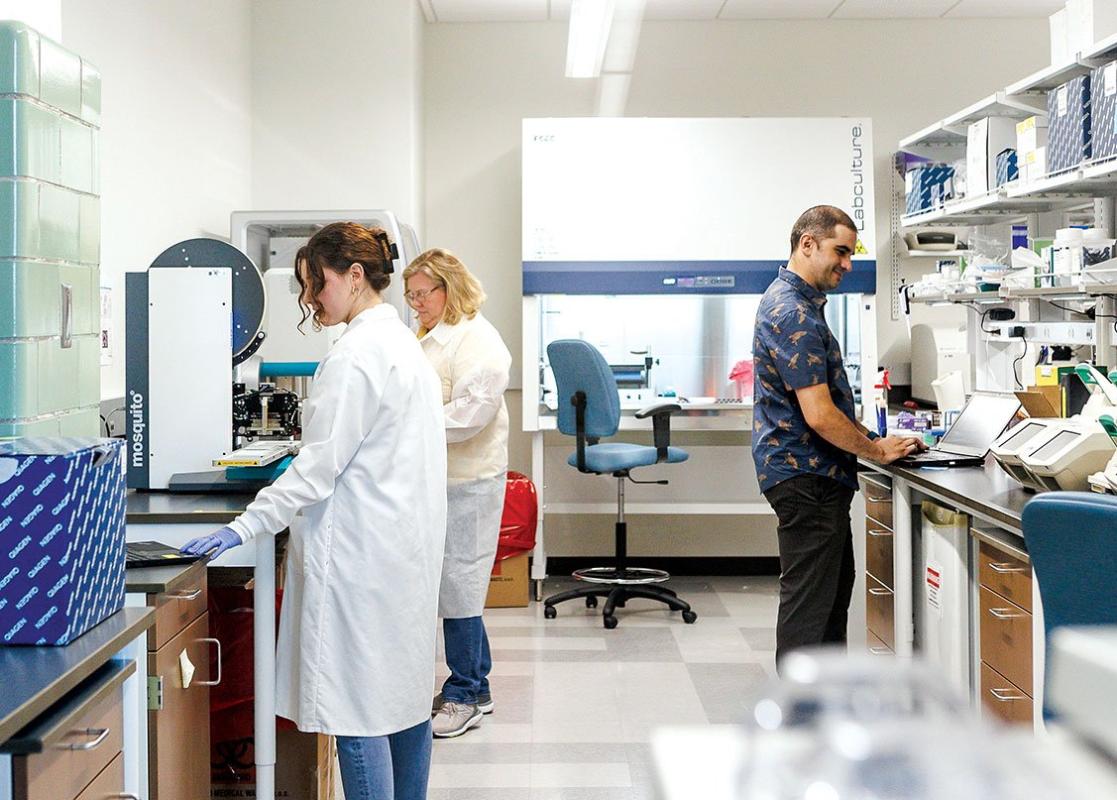 three scientists working at two lab benches