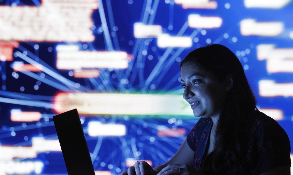 Monica Agrawal sitting at laptop with a futuristic background