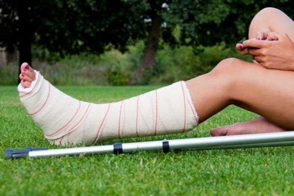 person sitting on grass with casted foot and crutch