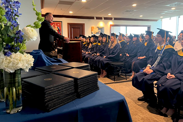Graduates sitting in chairs in their regalia listing to the chair speak at graduation