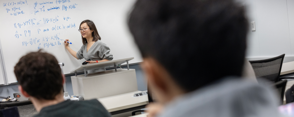 Instructor writing on whiteboard with students in the foreground