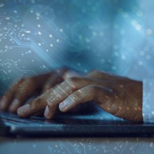 Photo of hands at a laptop overlaid with computer code 